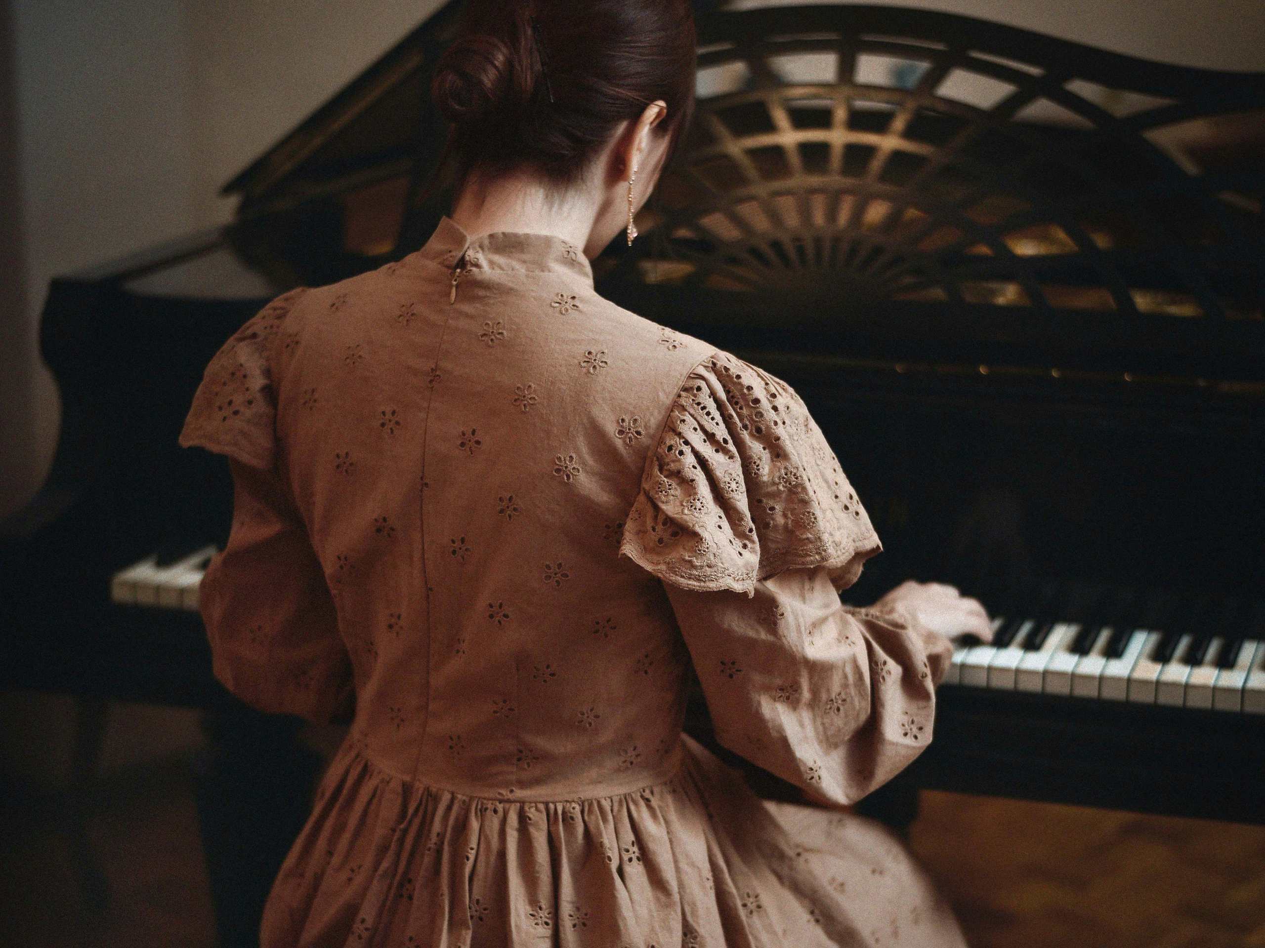 Femme de dos en robe d'époque assise à un piano