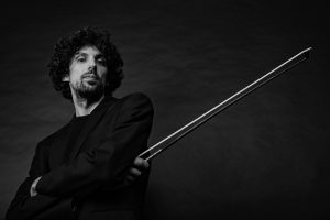 Black-and-white portrait of cellist Daniel Claret holding his bow, arms crossed