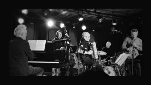 Le quintette de Daniel Mille, avec piano, contrebasse, accordéon, batterie et saxophone, en spectacle sur scène, photo noir et blanc