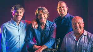 Jean-Pierre Zanella tenant son saxophone entouré de son quartet, éclairage bleu et mauve