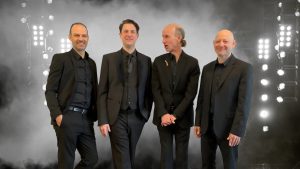 John Roney and his quartet, in black suits, posing on stage in a smoky atmosphere